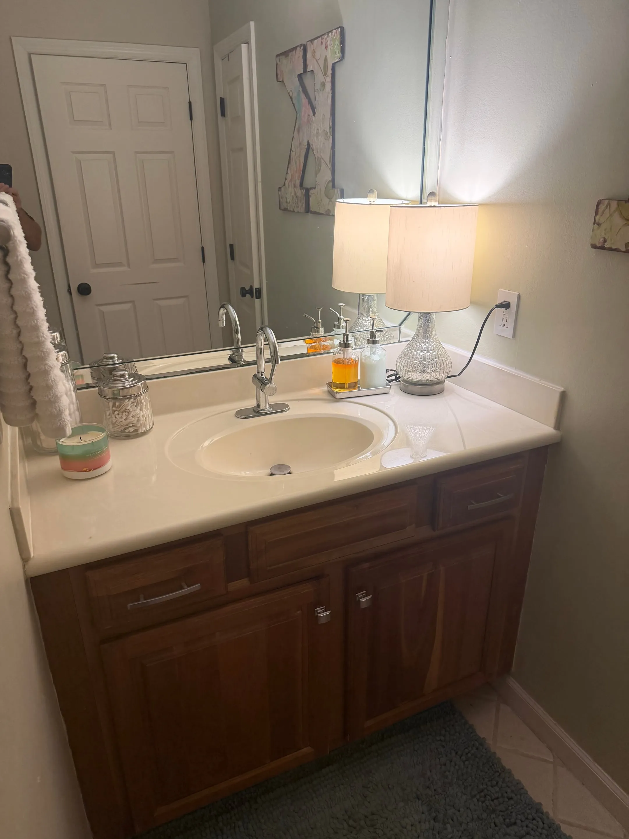 Bathroom vanity with wood cabinets, a white counter, and a large mirror.
