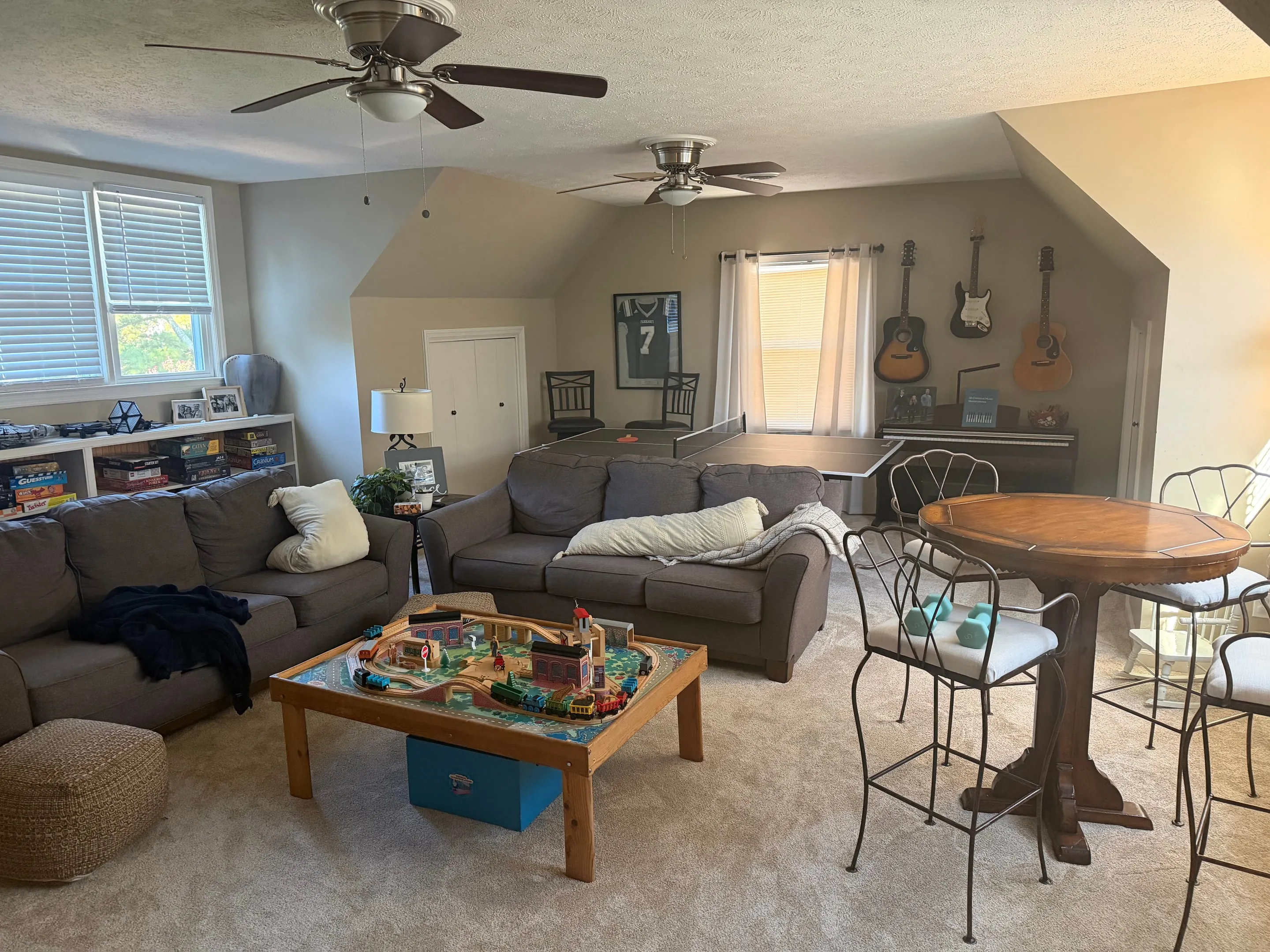 Large carpeted bonus room with two sofas, two ceiling fans, and windows on two walls.