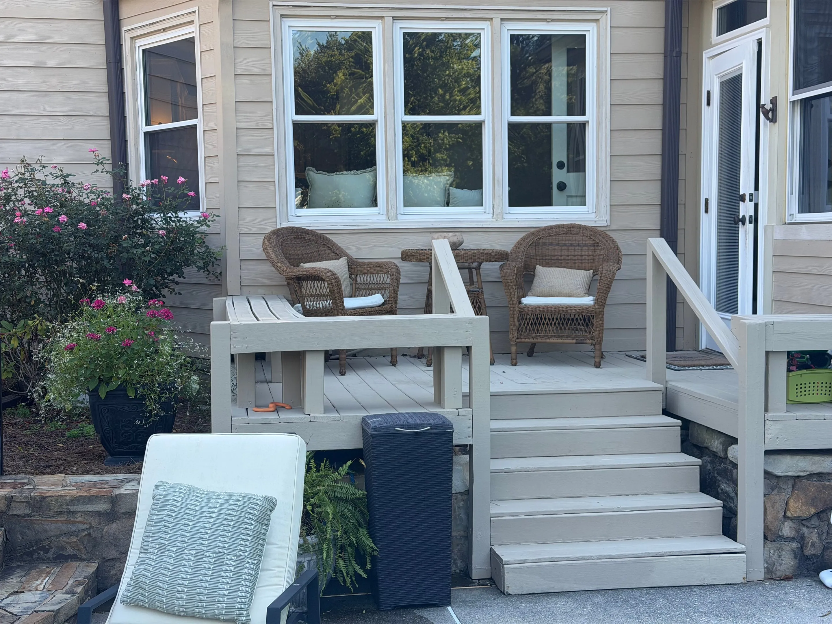 Wooden deck with two wicker chairs and steps down to the pool deck.