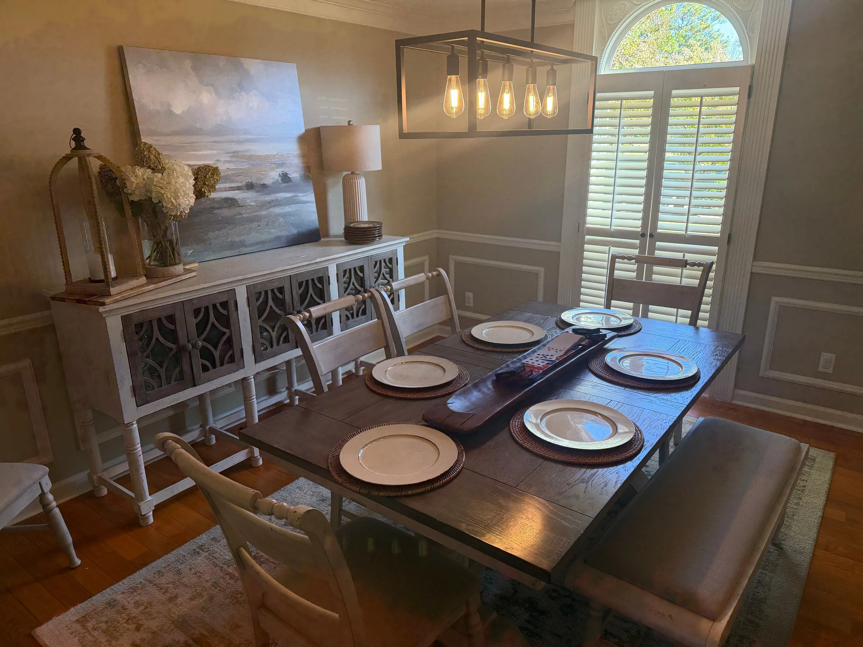 Dining room with wainscoting, a sideboard, a pendant light, and an arched window with shutters.