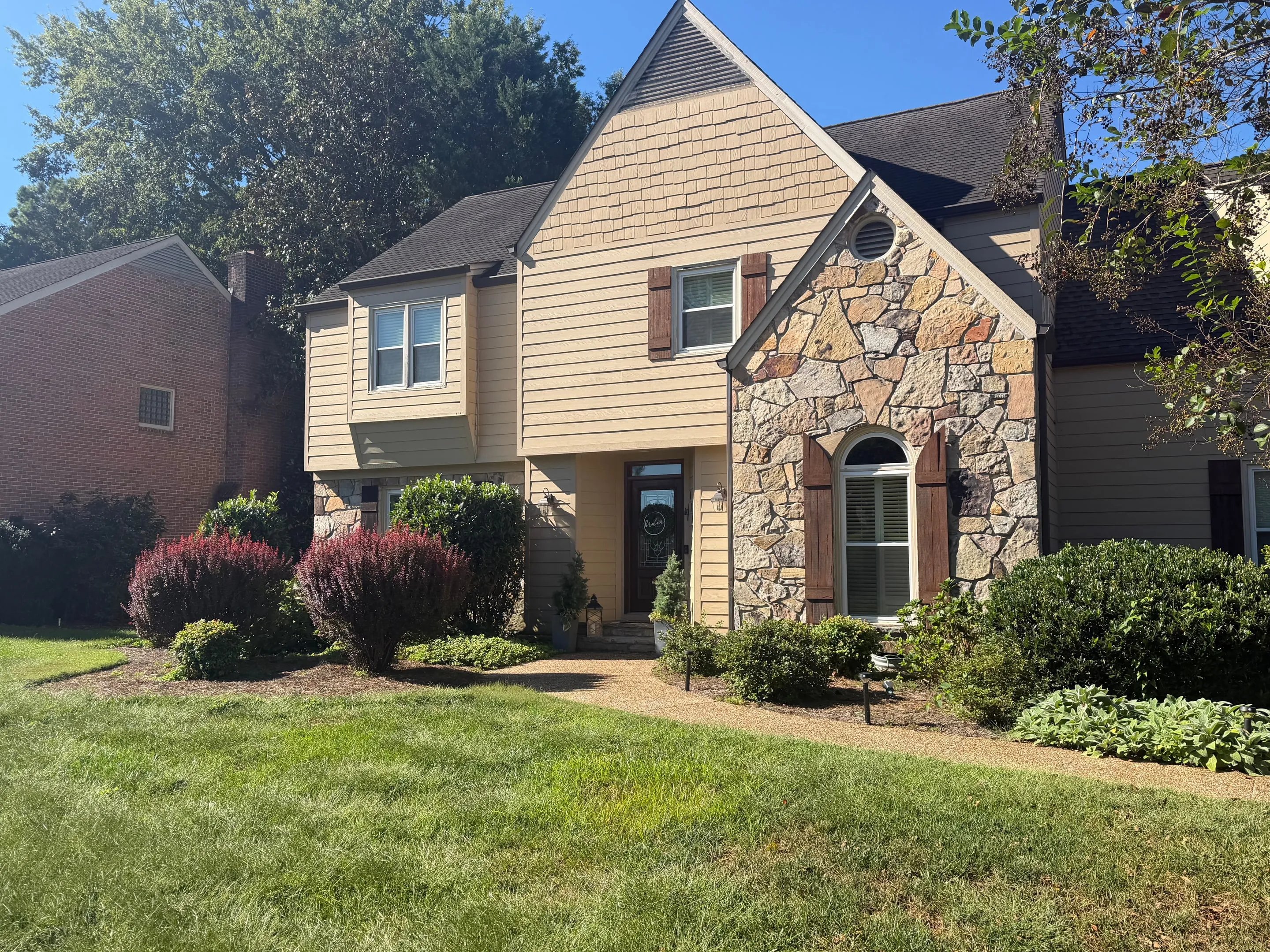Front door, arched window, and stone gable with shrubs along the walkway.