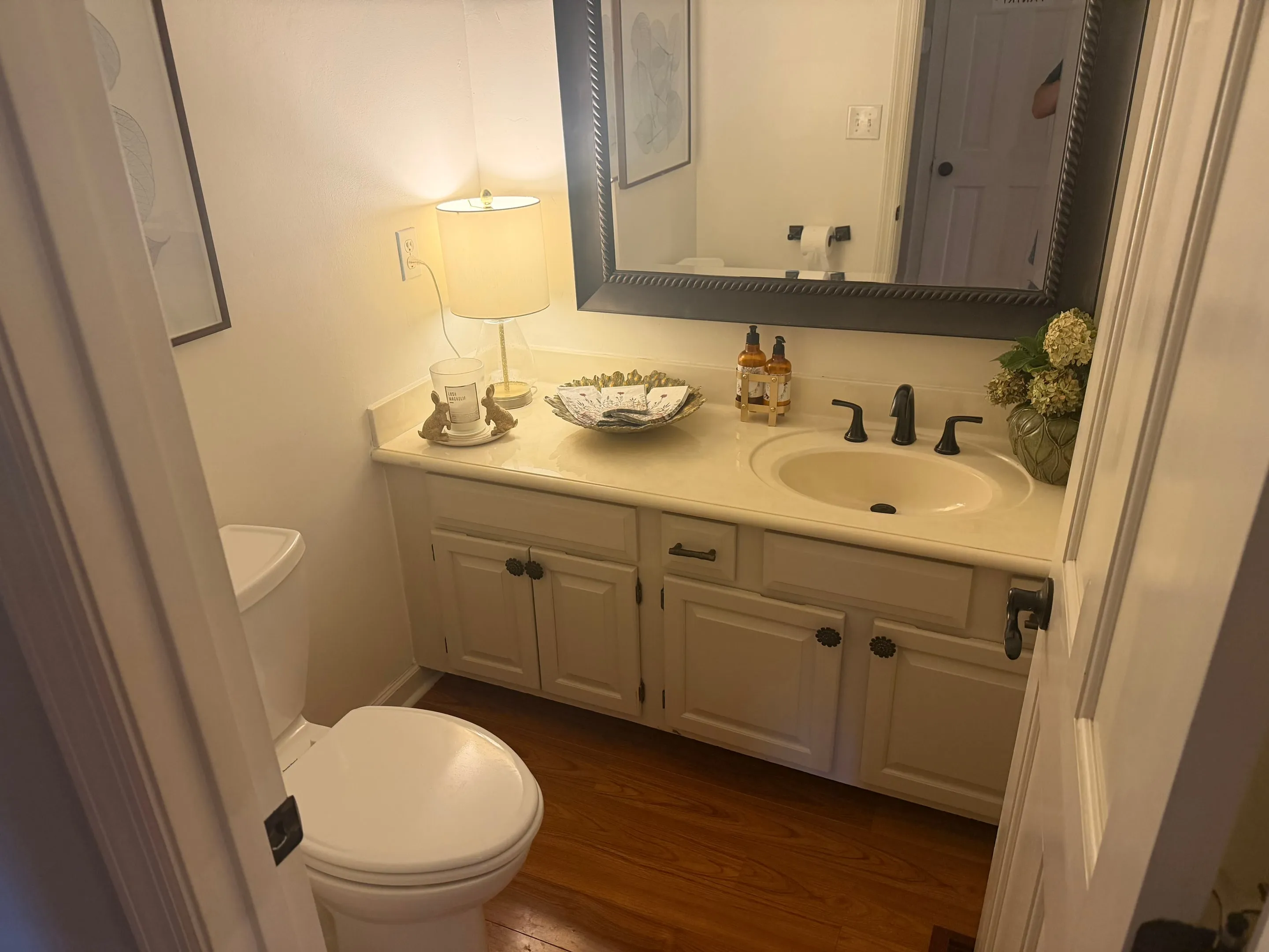Half bath with a white vanity, framed mirror, and hardwood floor.