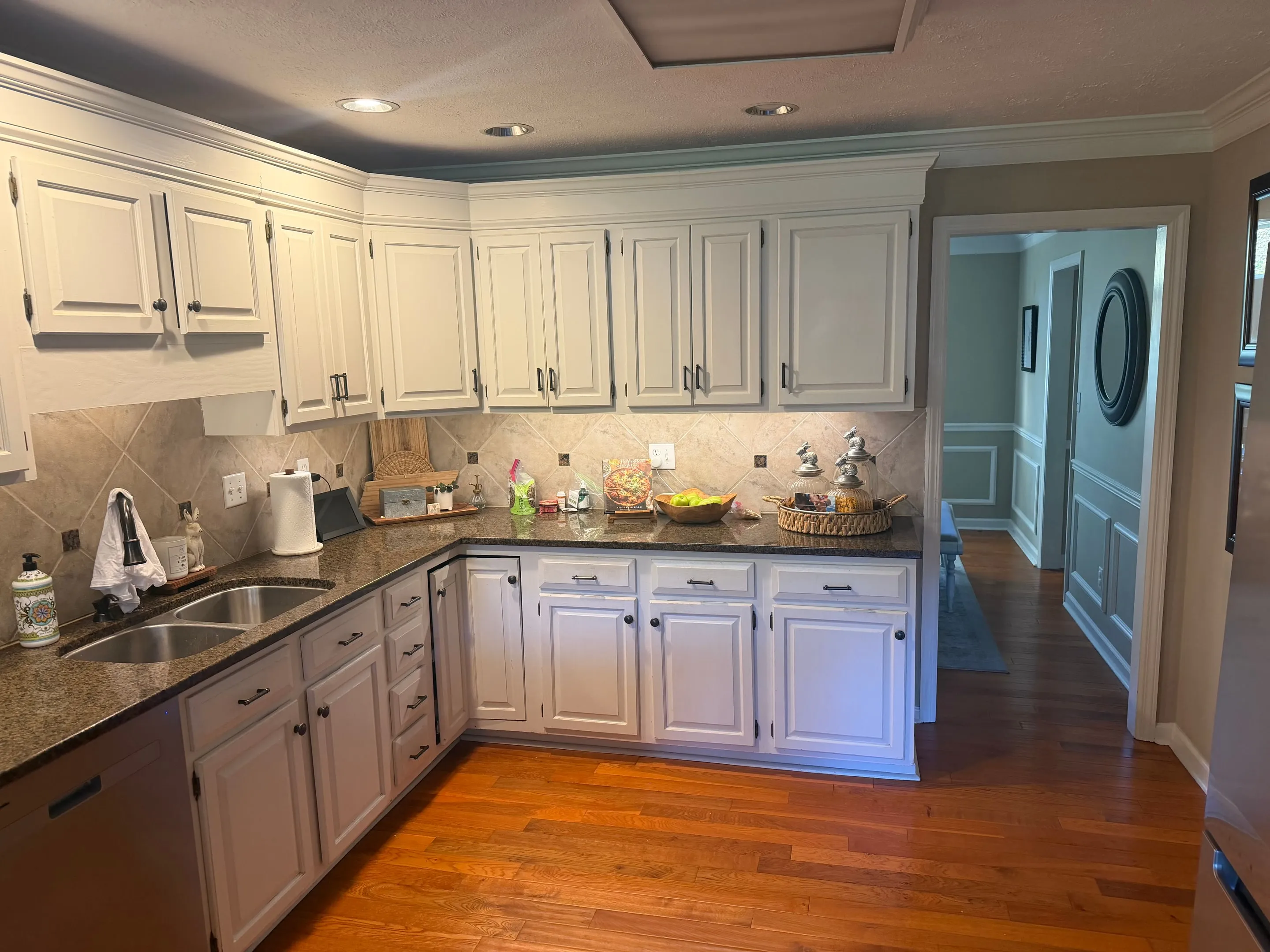 L-shaped kitchen with white cabinets, dark stone counters, a tile backsplash, and hardwood floors.