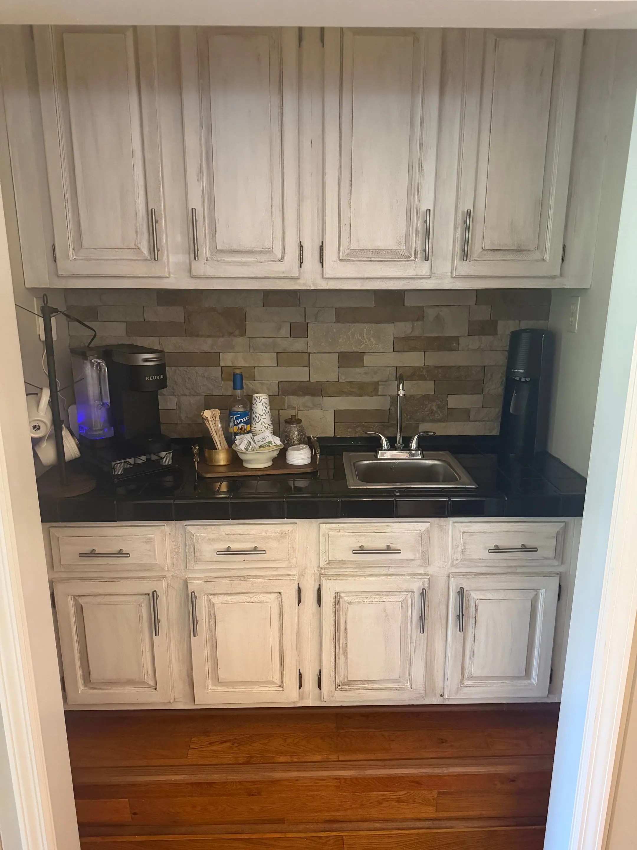 Wet bar with white cabinets, a dark counter, a small sink, and a tile backsplash.