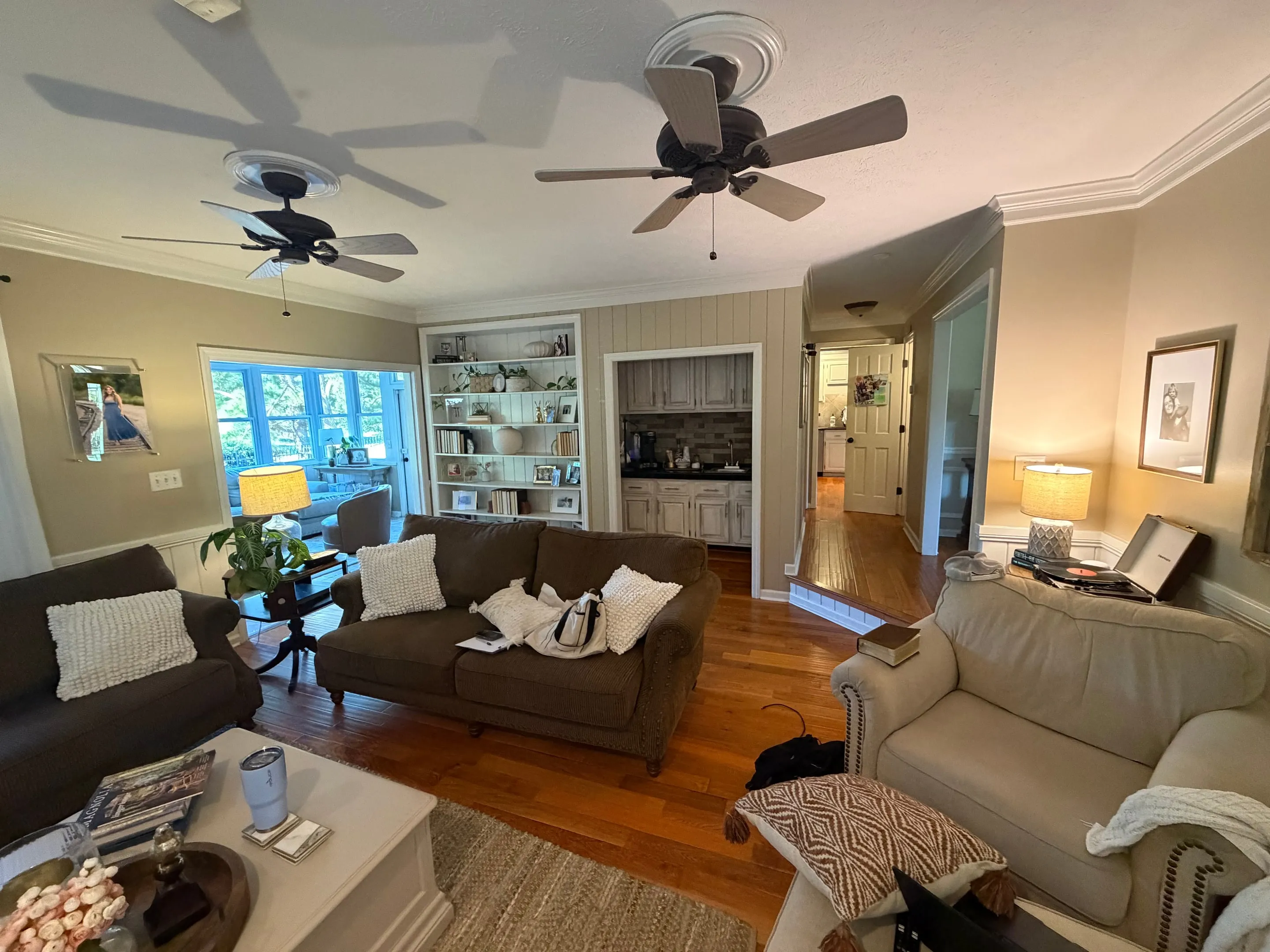 Living room with two sofas, hardwood floors, two ceiling fans, built-in shelves, and a wet bar alcove.