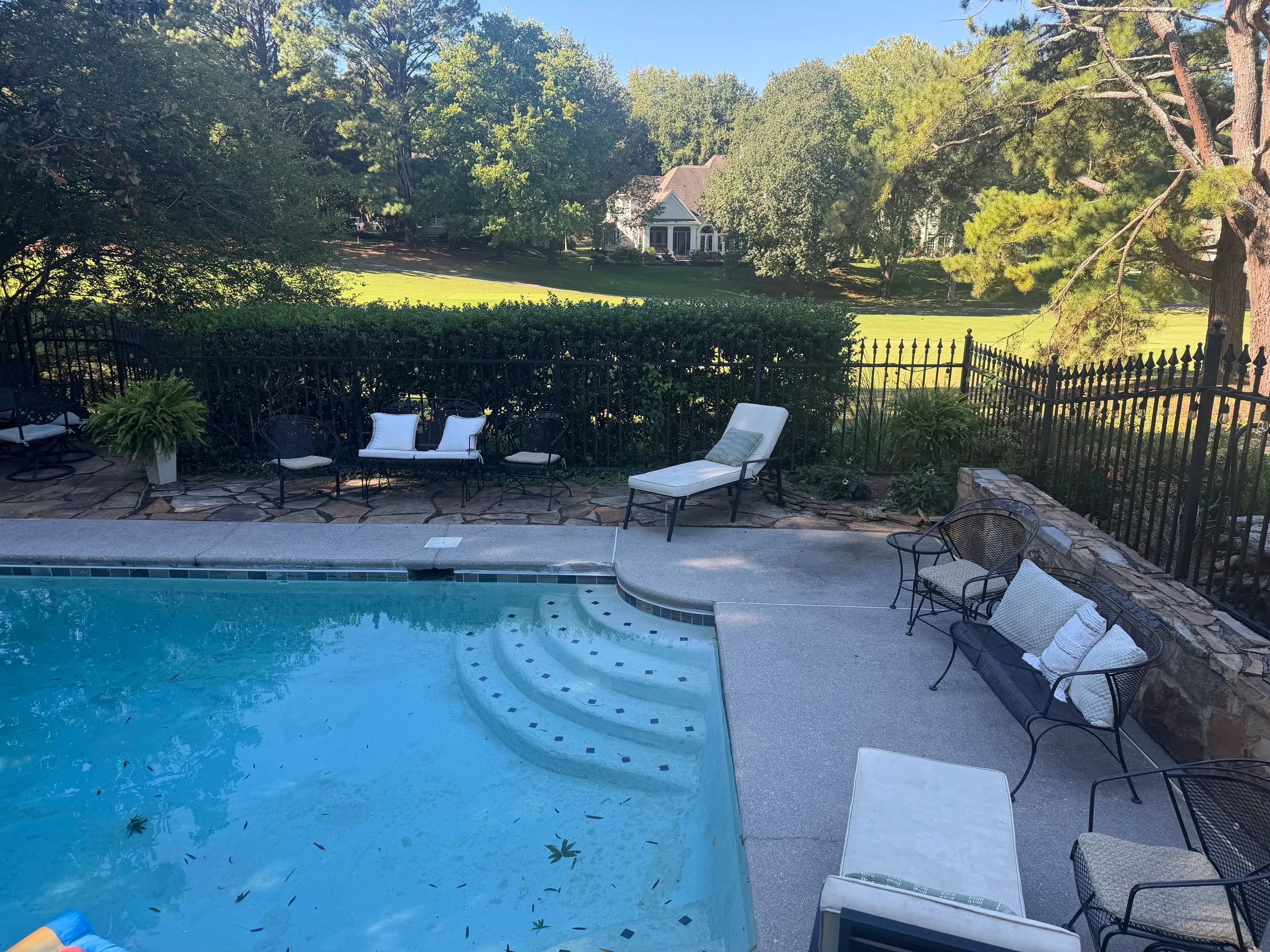 Curved pool steps with lounge chairs and benches on the patio beyond.