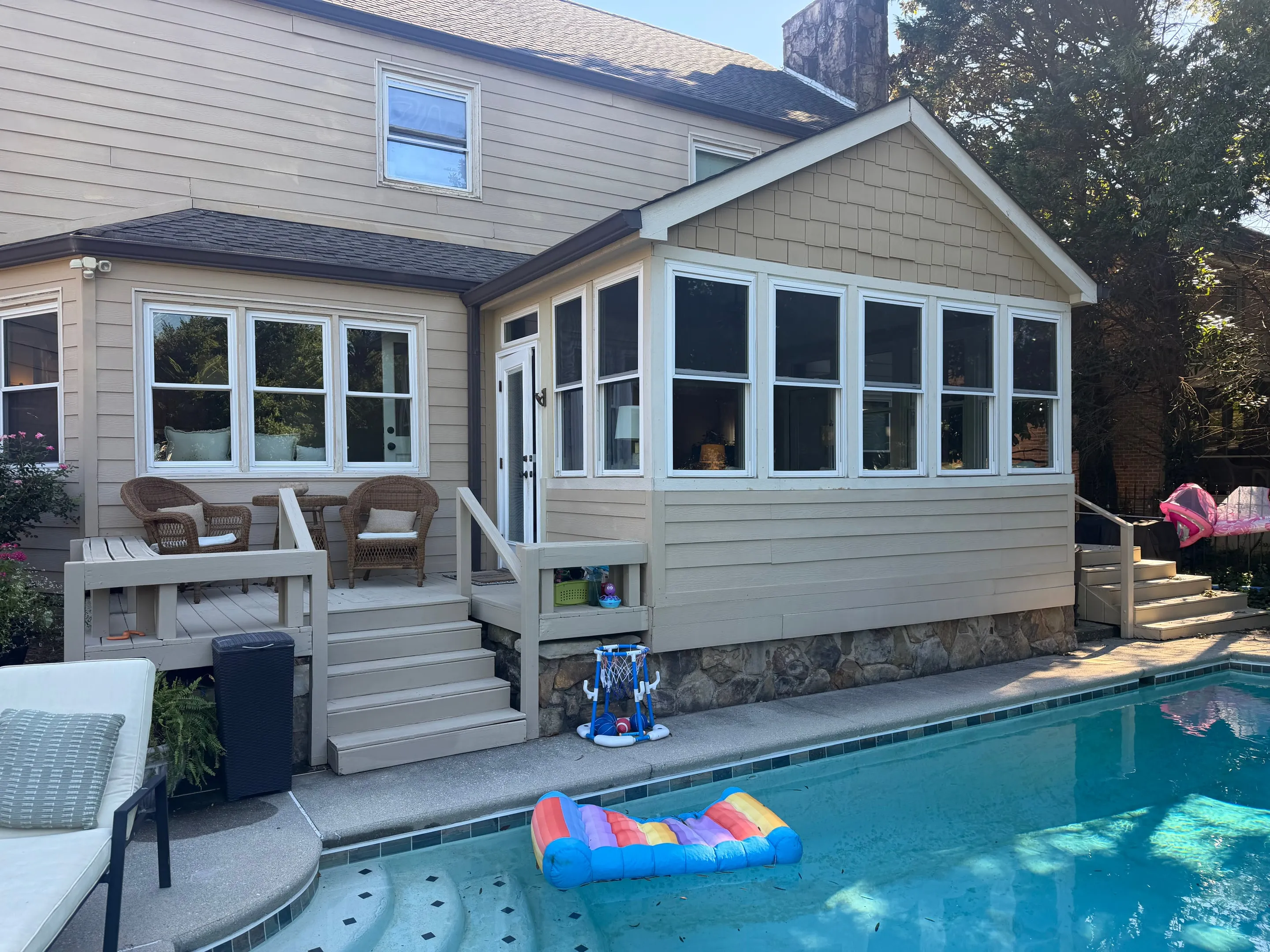 Rear of the house showing the sunroom, a wooden deck with steps, and the pool in the foreground.