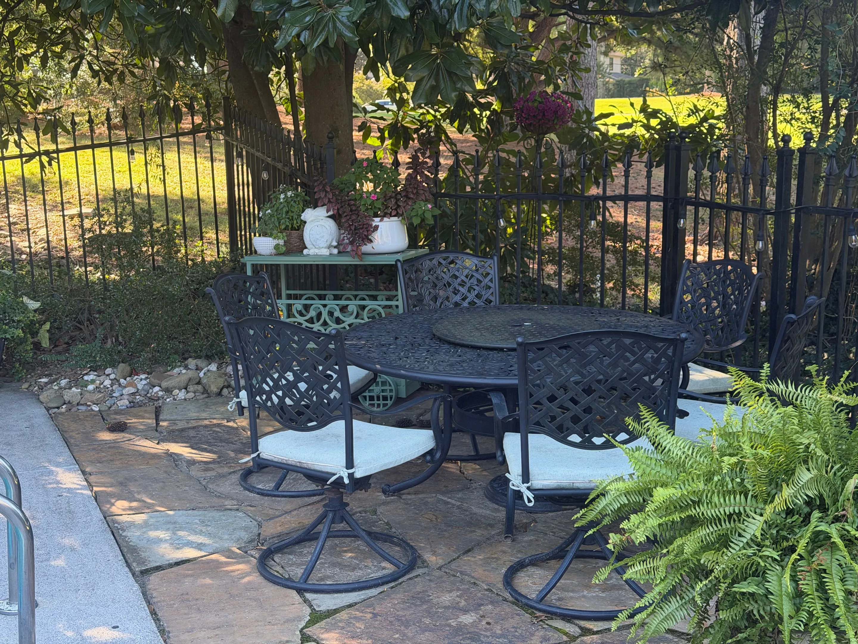 Round iron table and chairs on a flagstone patio under a magnolia tree.
