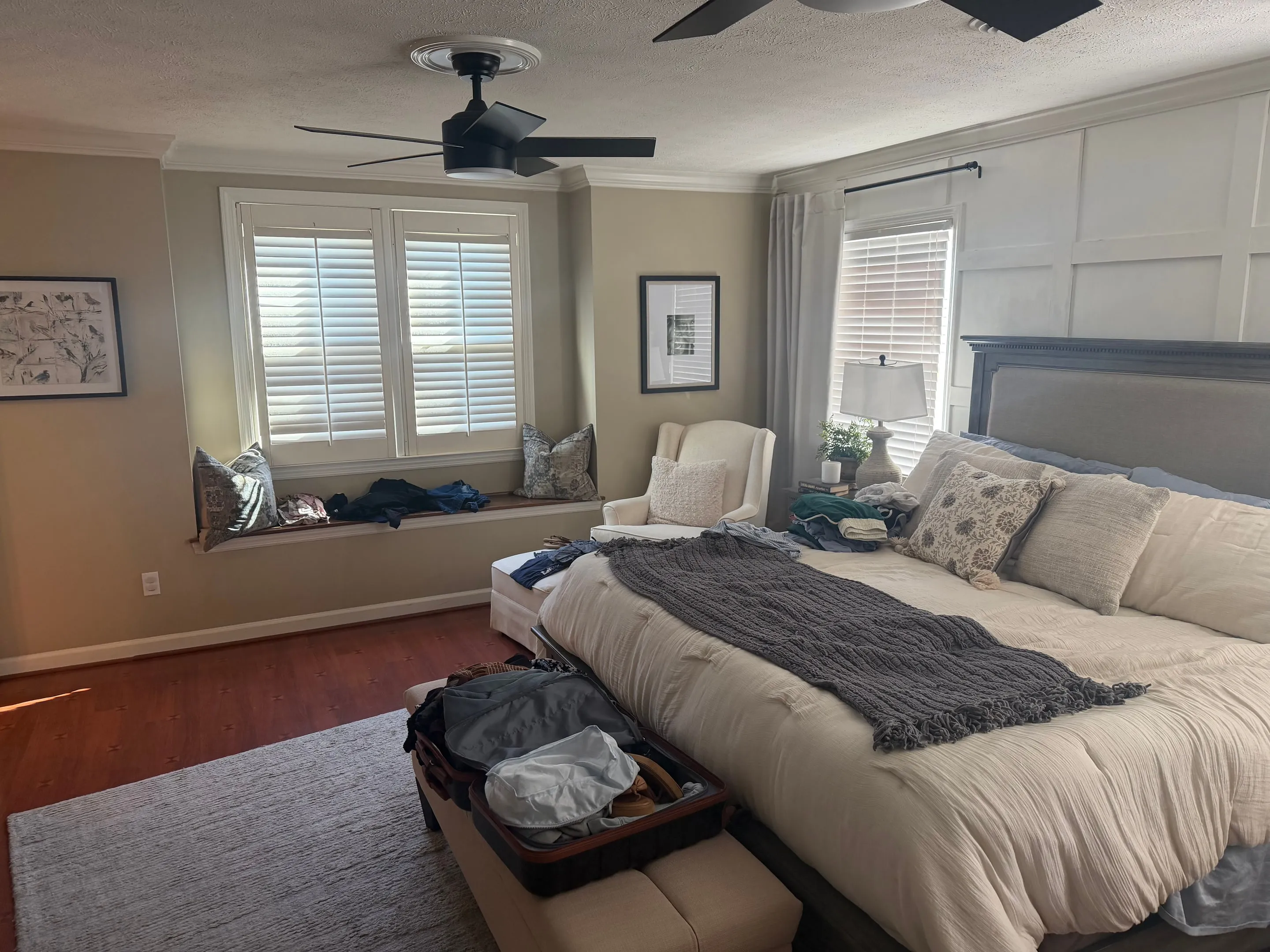 Window seat under two windows with plantation shutters, next to the bed.