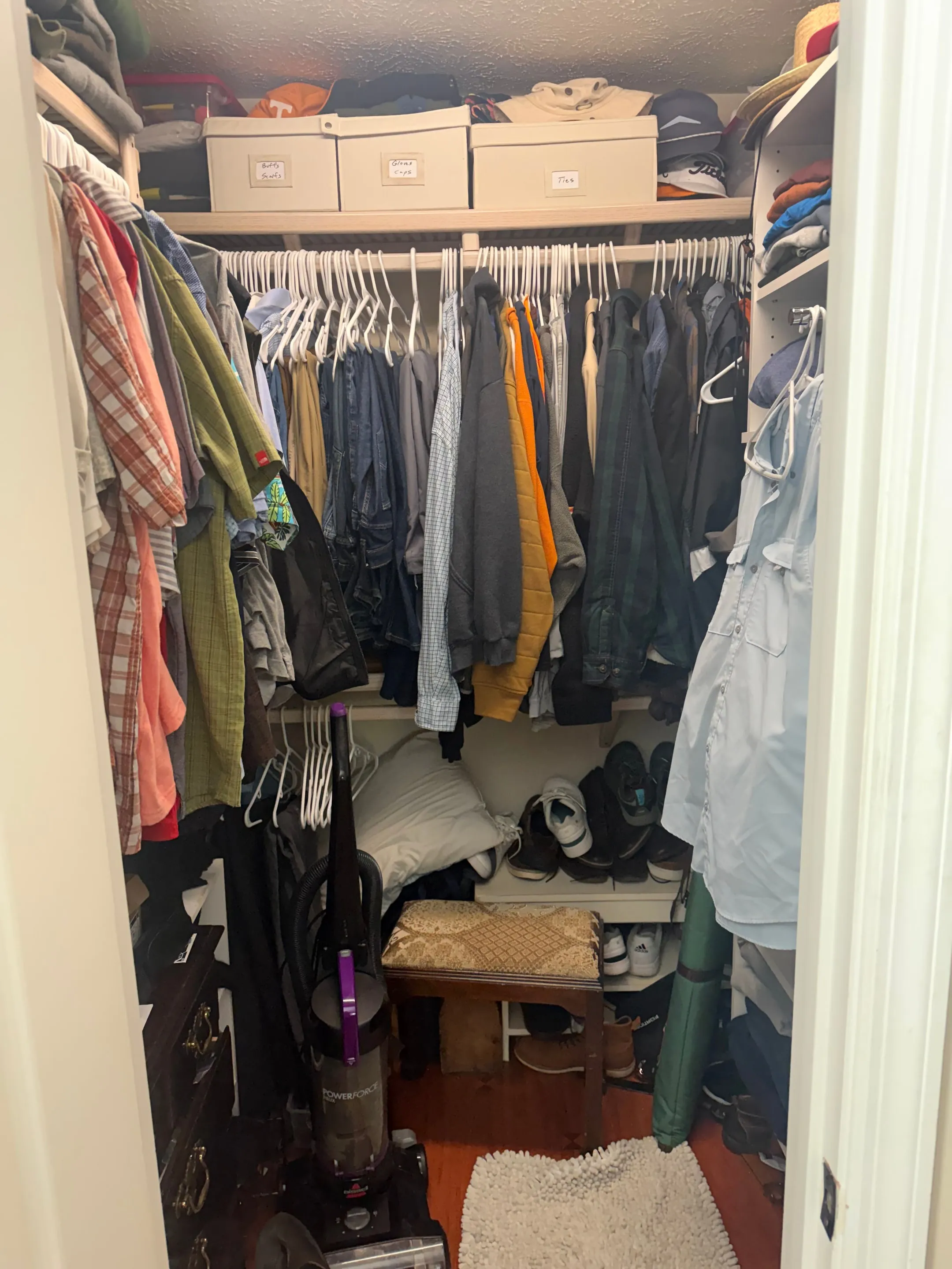 Walk-in closet with hanging rods on two walls and upper shelves.