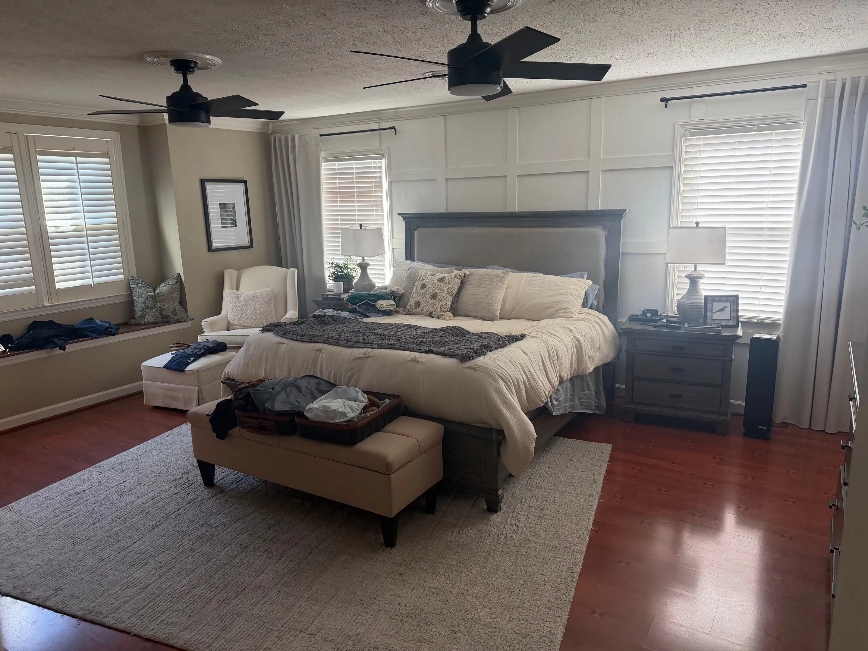 Primary bedroom with a paneled accent wall behind the bed, two ceiling fans, and a window seat.